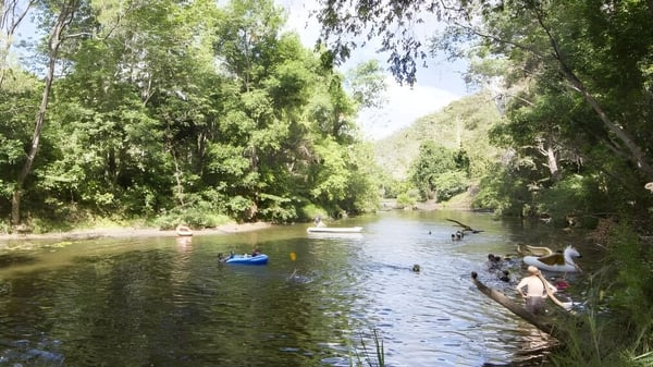Estudiantes de la MacGregor State High School disfrutan de actividades acuáticas como nadar y pasear en bote en un tranquilo paisaje fluvial.