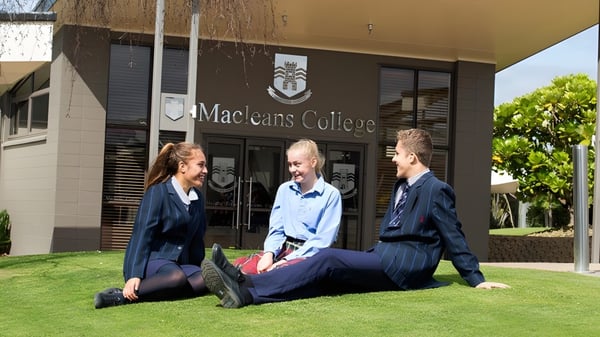 Tres estudiantes están sentados en la pradera frente al edificio del Macleans College.