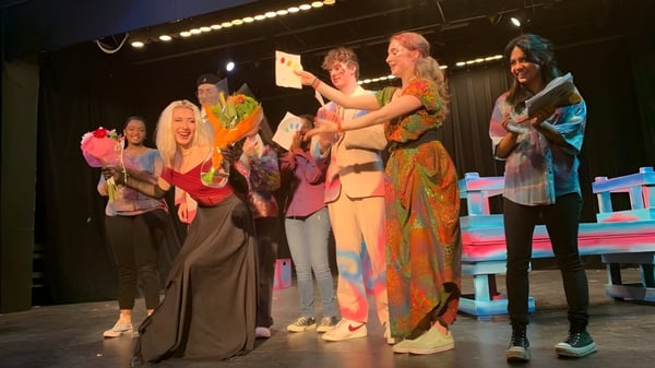 Estudiantes de la Maharishi School están en trajes coloridos en el escenario durante una actuación.