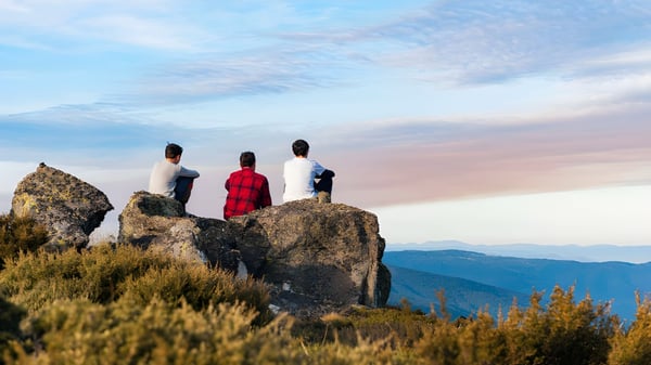Tres personas están de pie sobre una roca y miran el paisaje montañoso desde la Malanda State High School.