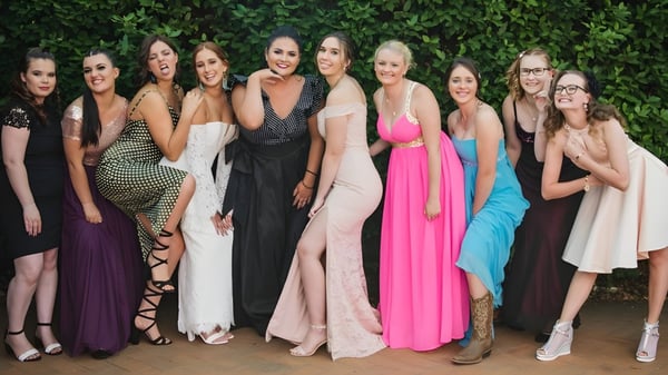 Un grupo de estudiantes de la Maleny State High School posan frente a un follaje verde en varios vestidos festivos.