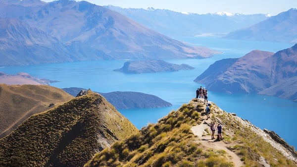 Dos estudiantes del Manawatu College están en una caminata en un saliente rocoso con vista a un lago de montaña turquesa.