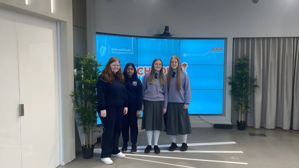 Un grupo de jóvenes estudiantes de la Manor House School está vestida de manera informal frente a una gran pantalla azul en un interior con plantas.