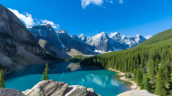 Un tranquilo lago de montaña turquesa frente a picos nevados y bosques perennes en el campus del Appleby College.