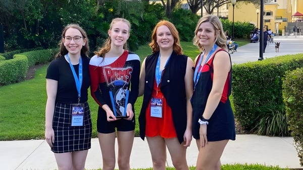 Cuatro estudiantes de la Maple Ridge Secondary School están juntas al aire libre frente a vegetación verde y un camino pavimentado.
