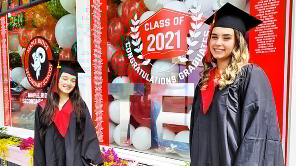 Dos estudiantes en toga de graduación están frente a una decoración para la Clase de 2021 en el campus de la Maple Ridge Secondary School.