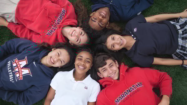 Un grupo de estudiantes de la Maranatha High School está acostado en círculo sobre el césped y conversando.