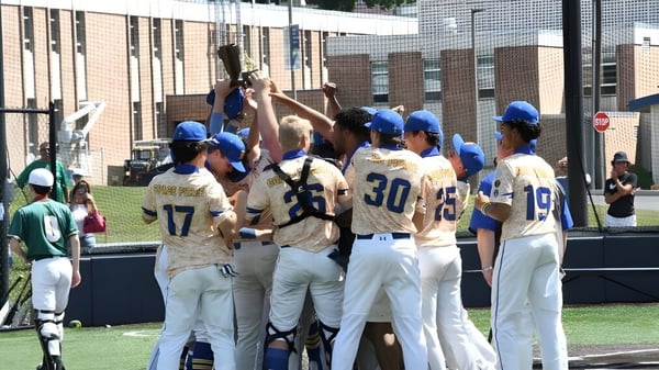 Un grupo de estudiantes de béisbol en uniforme está de pie en el campo frente al edificio de la Marian Catholic High School.