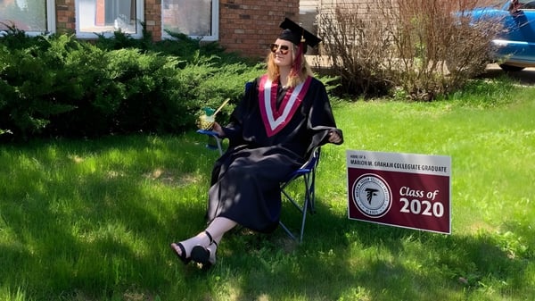 Una absolventa en togas está frente a un cartel que dice Class of 2020 en el campus de Marion M. Graham Collegiate.