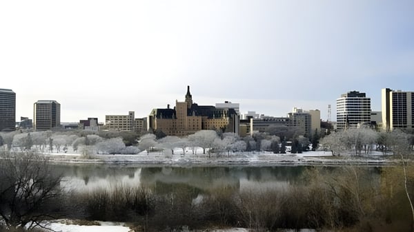 Un lago congelado frente al paisaje urbano nevado con altos edificios y una construcción parecida a un castillo en el fondo cerca de Marion M. Graham Collegiate.