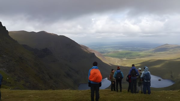 Un grupo de caminantes está de pie sobre una roca con una amplia vista del valle montañoso en el campus del Marist College.