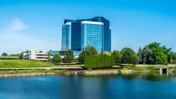 El moderno edificio de vidrio y acero de la Markham District High School se alza alto frente a un cielo despejado y rodeado de áreas verdes y agua.
