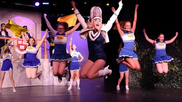 Un grupo de alumnas del Marlborough College se presenta en el escenario con trajes coloridos frente a un fondo iluminado.