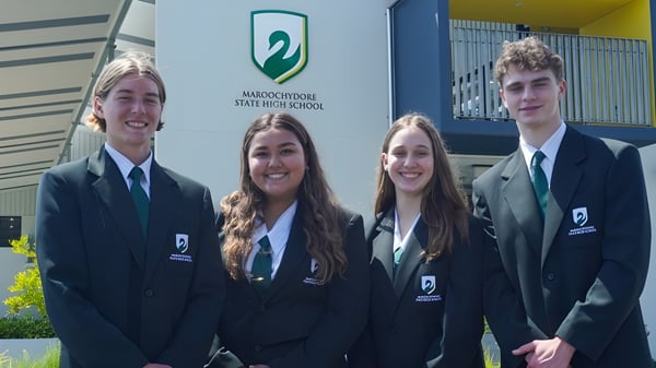 Cuatro estudiantes están frente al edificio de la Maroochydore State High School en uniformes escolares.