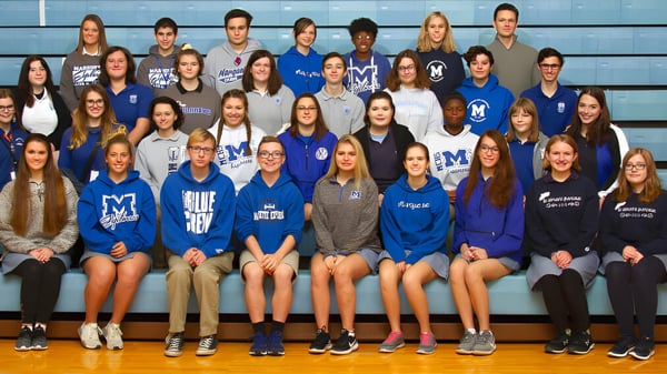 Un grupo de estudiantes en uniformes escolares azules y blancos posan en el gimnasio de la Marquette High School.