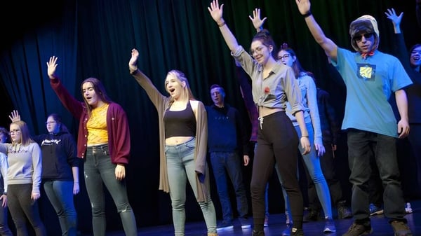 Estudiantes de la Marymount Academy International están en un escenario con los brazos levantados frente a un fondo oscuro.
