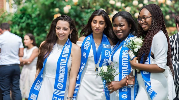 Estudiantes de la Marymount Academy International están afuera en un jardín verde y sonríen juntas.