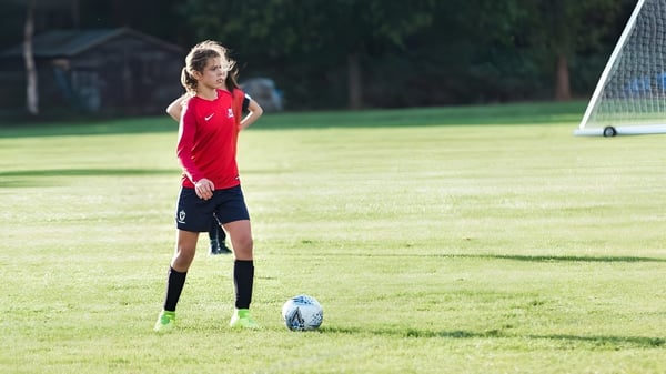 Una joven futbolista de la Marymount International School está en el campo con el balón en el pie frente a una portería.
