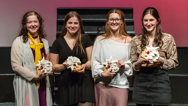 Cuatro estudiantes de la Massey-Vanier High School están con ramos de flores blancas frente a un fondo rosa y negro.