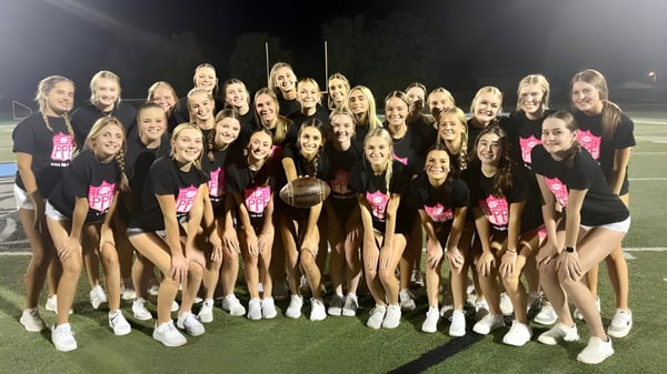 Las animadoras de la Mater Dei Catholic High School posan con uniformes uniformes en el campo deportivo de noche bajo luces brillantes.