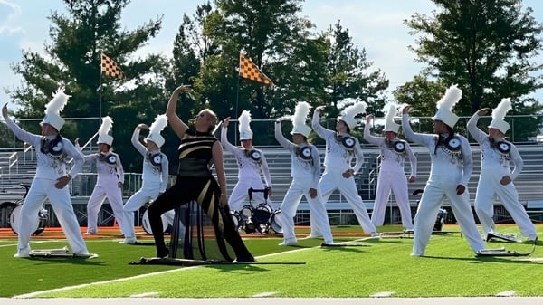 Un grupo de artistas en atuendos blancos y negros está en una pradera en el terreno de la Mater Dei Catholic High School.