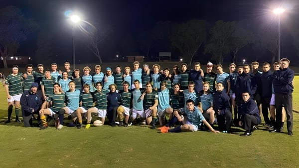Un gran grupo de estudiantes del Matthew Flinders Anglican College posan juntos en un campo deportivo iluminado por la noche.