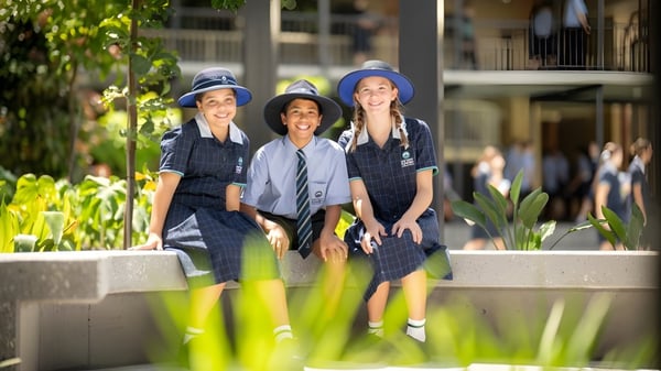 Tres estudiantes del Matthew Flinders Anglican College están juntos frente a un fondo de plantas verdes y sonríen.
