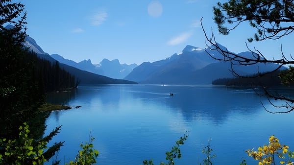 Un tranquilo lago alpino con un pequeño bote, rodeado de montañas y vegetación, cerca de la Maxwell Heights Secondary School.