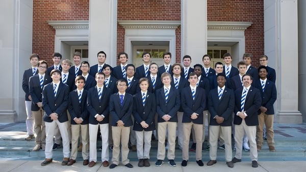 Un grupo de estudiantes de la McCallie School está frente a un edificio de ladrillo rojo con columnas y ventanas en forma de arco.