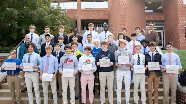 Un grupo de estudiantes de la McCallie School está frente a un edificio de ladrillo sosteniendo carteles y certificados.