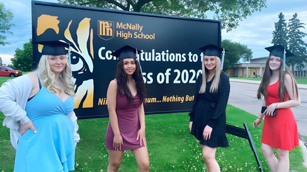 Cuatro alumnas posan frente a un cartel con felicitaciones para la clase de graduación 2022 de la McNally High School.