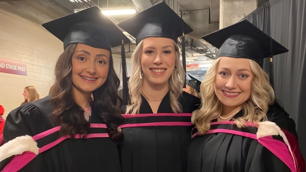 Tres graduadas de la Memorial University posan en sus togas y birretes en un pasillo.