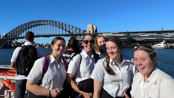 Un grupo de jóvenes estudiantes de la Menai High School posan frente al Puente de la Bahía de Sídney con el horizonte de la ciudad de fondo.