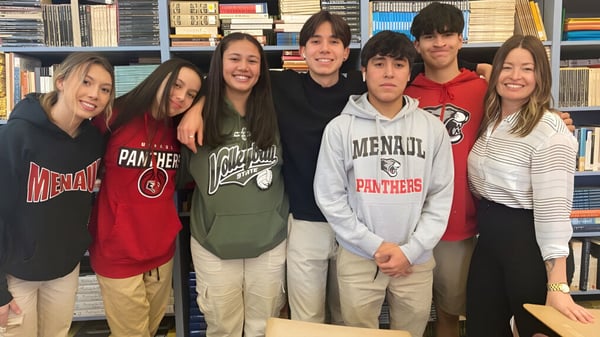 Un grupo de estudiantes de la Menaul School posan juntos frente a estanterías de libros en una biblioteca escolar.