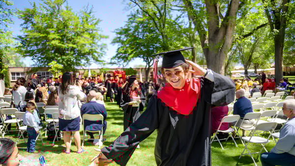 Un graduado de la Menaul School está en una capa y toga negras frente a un grupo de personas en un campo verde.