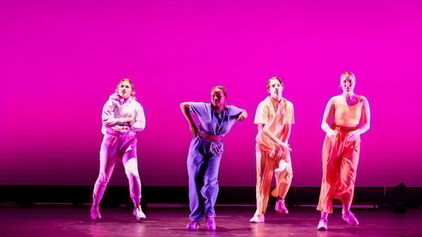 Cuatro estudiantes de la Mercersburg Academy están en trajes coloridos frente a un fondo rosa durante una actuación.