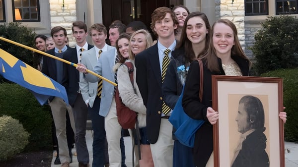 Un grupo de estudiantes de la Mercersburg Academy está frente a un edificio sosteniendo un retrato enmarcado.