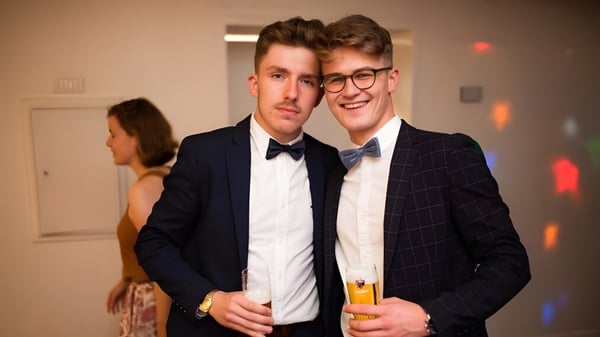 Dos jóvenes en traje formal están en una fiesta en el campus de la Merchiston Castle School sosteniendo bebidas.
