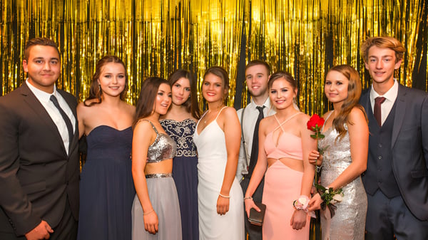 Un grupo de estudiantes bien vestidos está frente a un brillante fondo dorado en el campus de la Mercury Bay Area School.