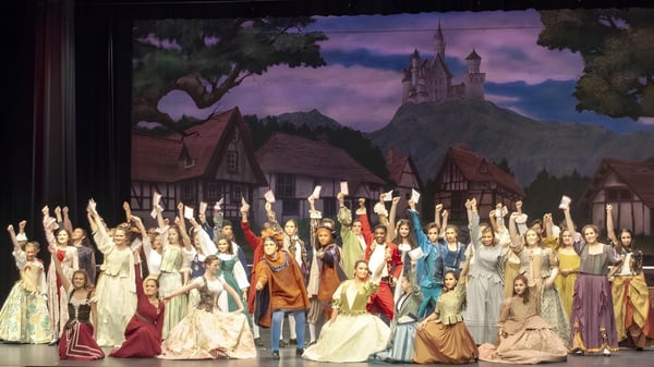 Estudiantes de la Mercy Secondary School Ballymahon están frente a un fondo con un imponente castillo y un cielo dramático.
