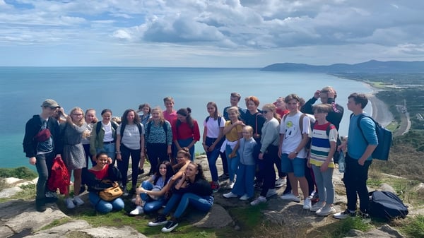 Estudiantes de la Mercy Secondary School están en una roca mirando el paisaje costero con agua y montañas.
