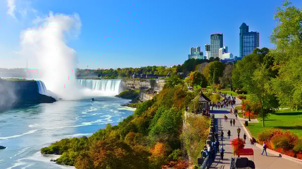 Una cascada fluye hacia un río frente al telón de fondo de áreas verdes y rascacielos cerca de la Merivale High School.