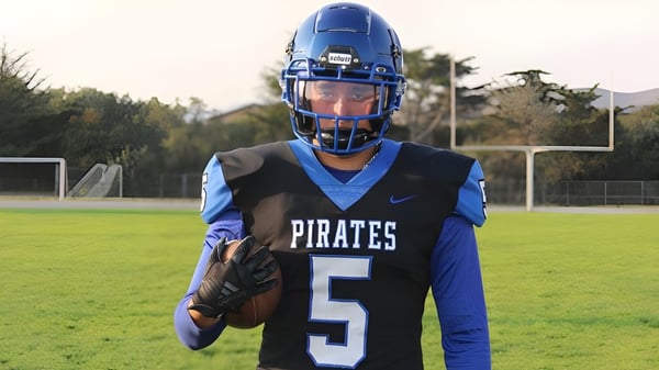 Un estudiante del Mesa Unified School District está en la camiseta de fútbol azul con el número 5 en un campo verde frente a un poste de gol.