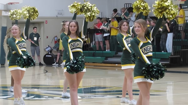 Animadoras de la Metro East Lutheran High School están en uniformes verde-amarillos en la cancha de baloncesto frente a los espectadores.