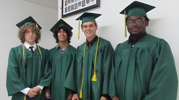 Cuatro estudiantes en togas de graduación verdes celebran su exitoso graduación en la Metro East Lutheran High School.