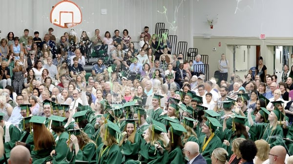 Graduados de la Metro International Secondary Academy están sentados en togas verdes en un auditorio durante la ceremonia de graduación.