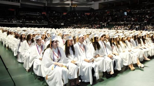 Estudiantes de la Miami Beach Senior High School llevan togas de graduación blancas en una ceremonia de graduación en un salón.