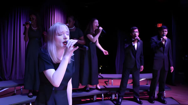 Una mujer en un vestido blanco canta en el escenario durante una actuación de la Miami Arts Charter School.