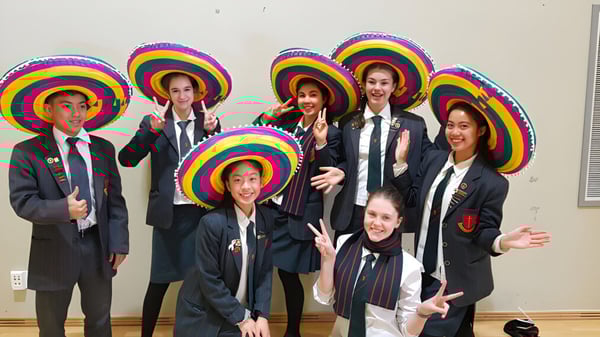 Un grupo de estudiantes de la Middleton Grange School posan juntos con sombreros y trajes coloridos frente a un fondo neutral.