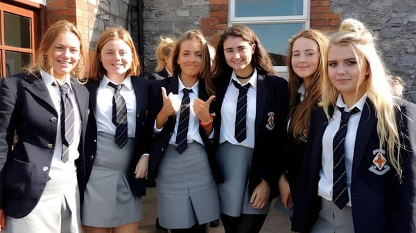 Un grupo de seis estudiantes en uniformes escolares está frente a un edificio de ladrillo en el campus del Midleton College.